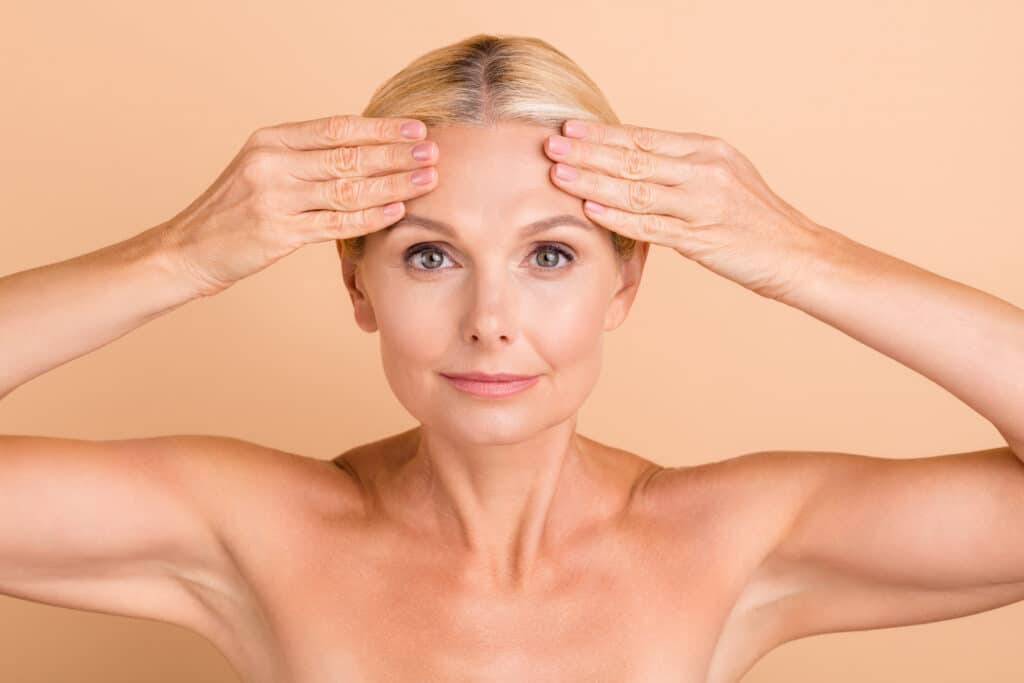 Older woman pulling her forehead taught to show her wrinkles, in need of a wrinkle relaxing injection.