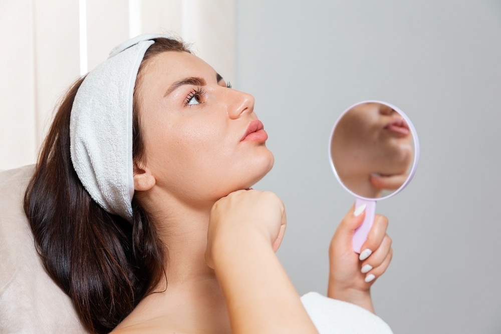 Woman touching her chin in the mirror after getting a PDO thread lift to tighten her face.
