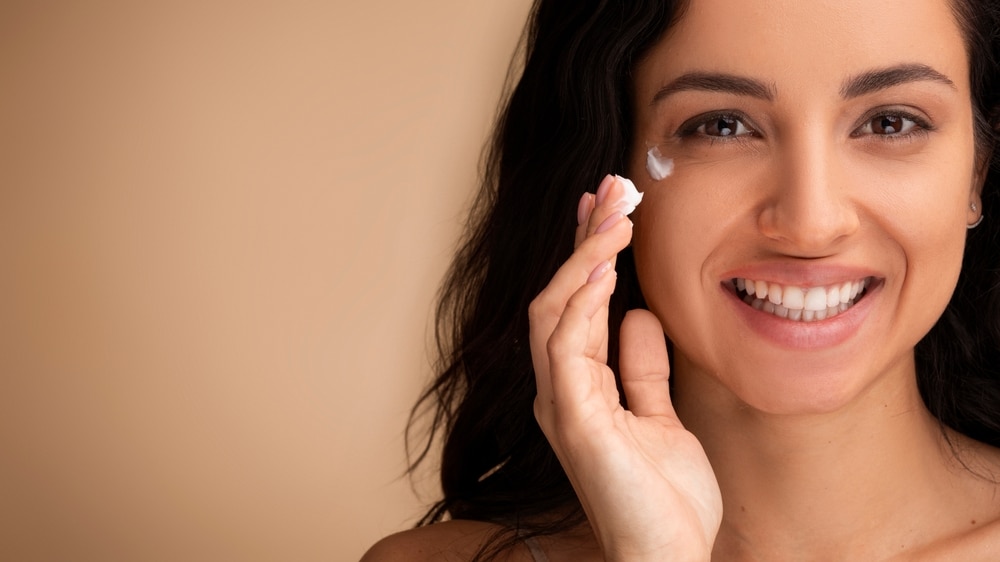 Smiling woman applying a peptide cream topically for improved health and wellness.