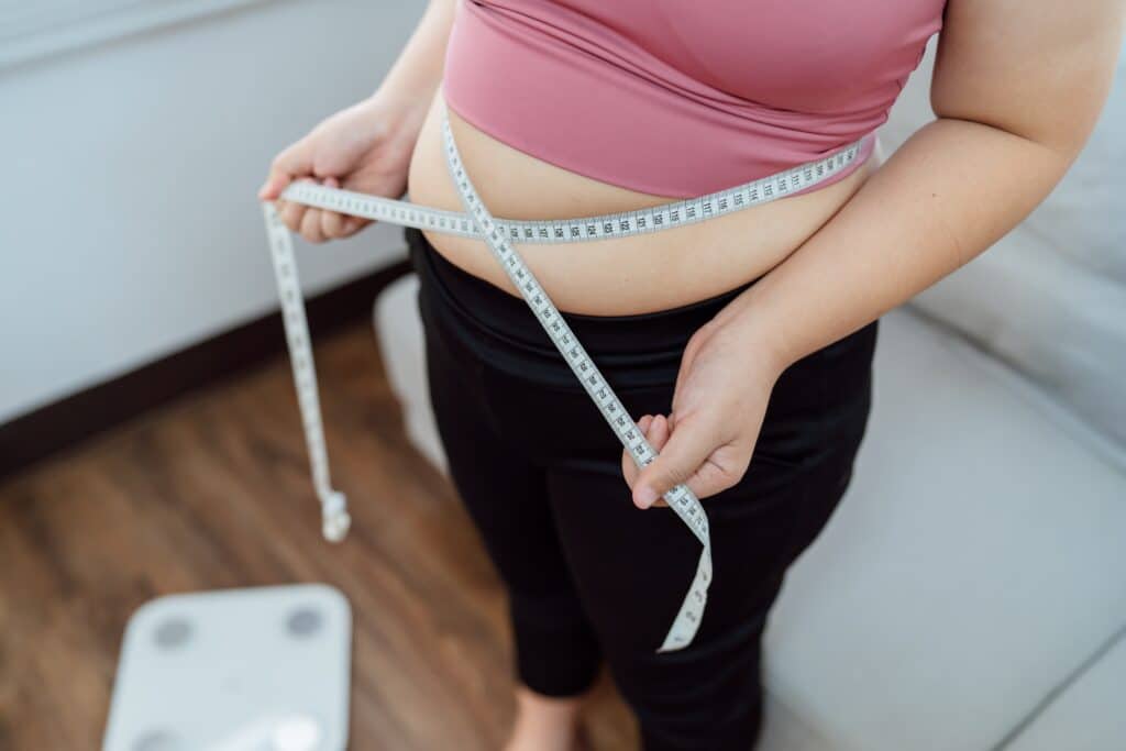Close up of a woman's stomach with a measuring tape pulled around it to show her issues with weight loss resistance.