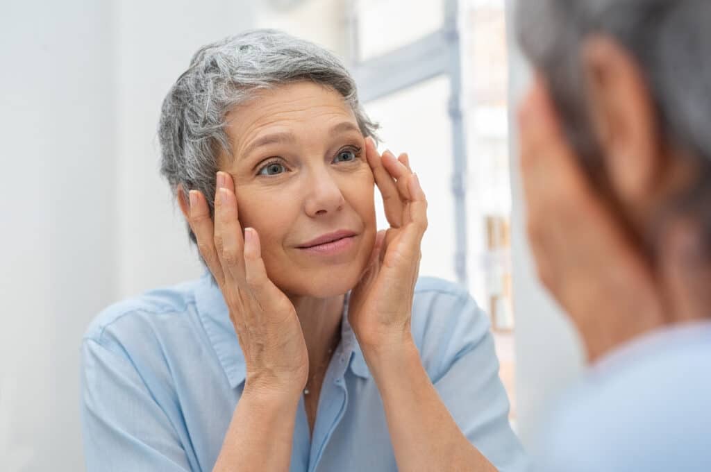 Older woman looking at her aging skin in the mirror, exacerbated by a vitamin B12 deficiency